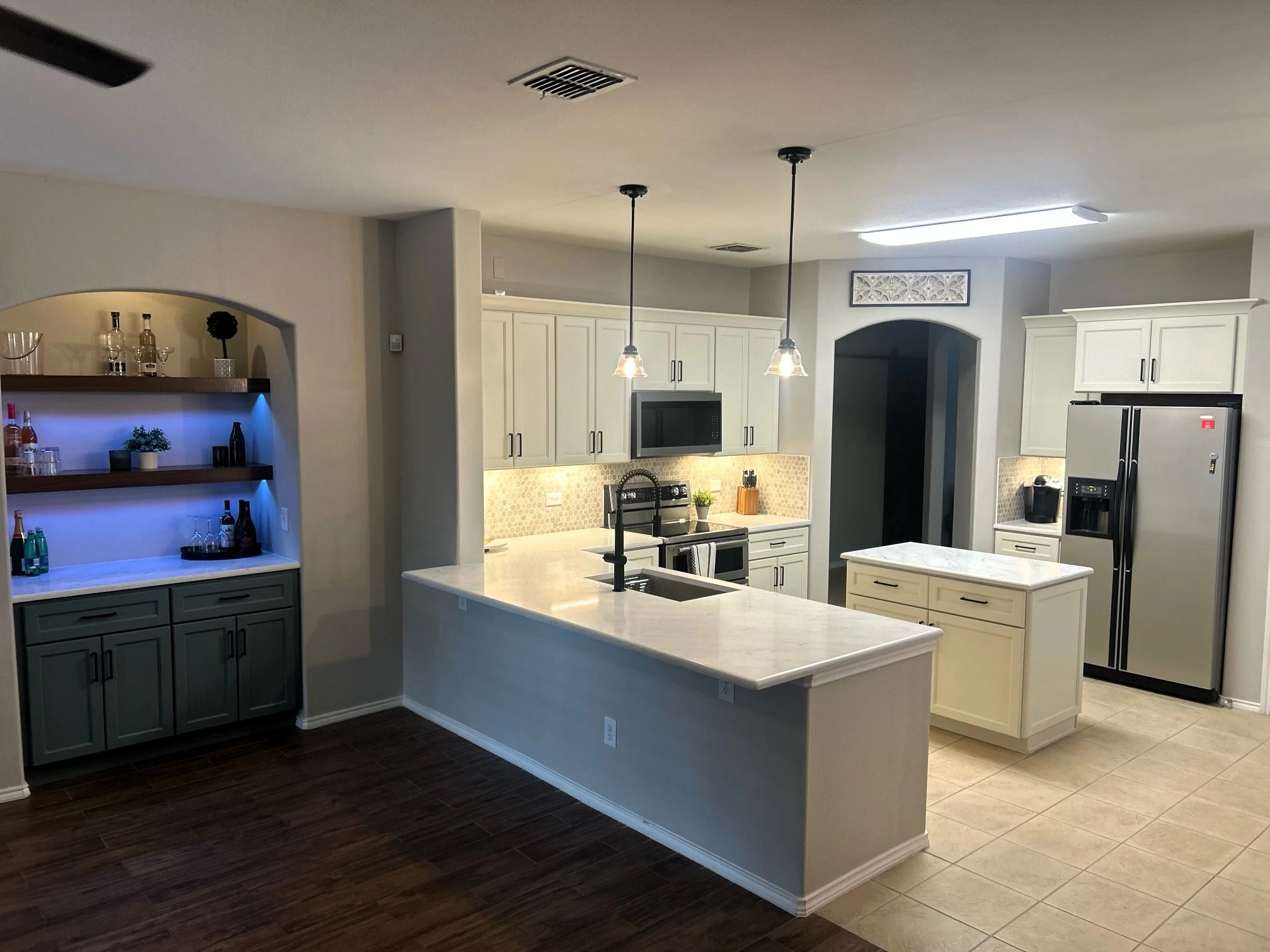 Remodeled kitchen with white cabinetry, an island and a custom illuminated bar